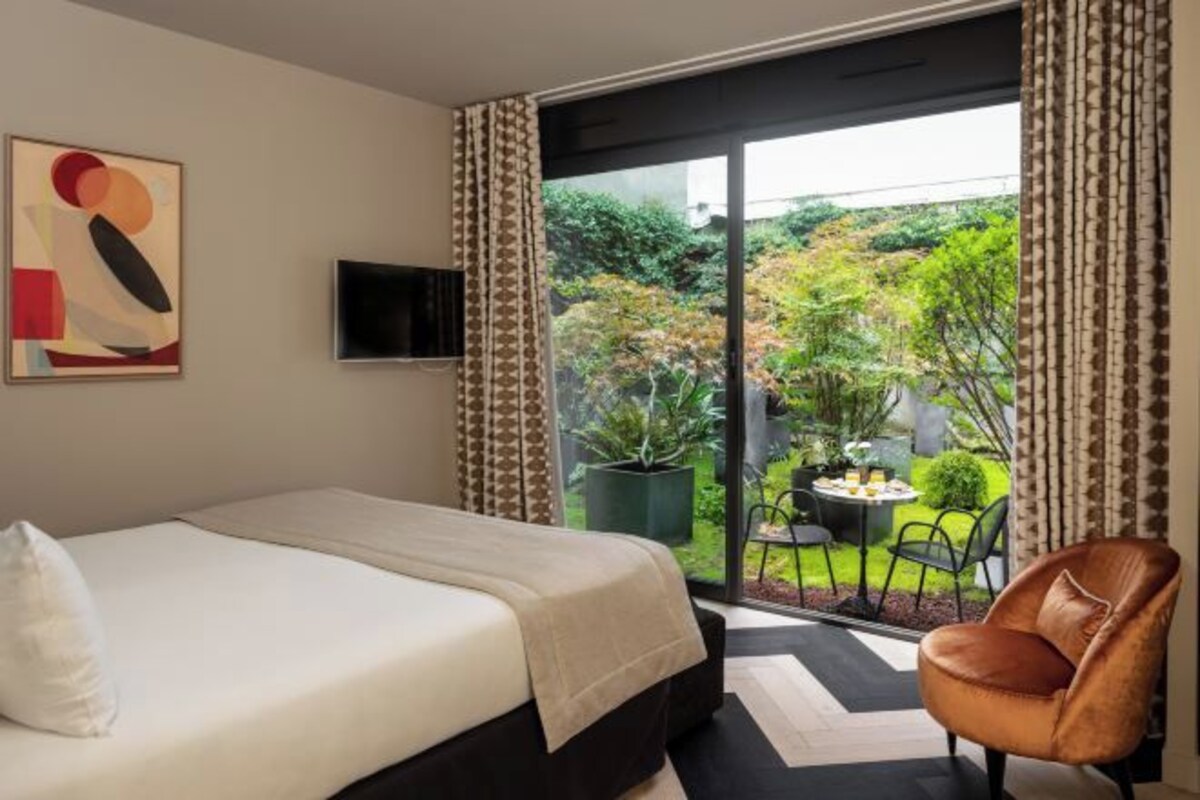 A bedroom with a bed, a TV, a view of a garden through a sliding door, and a chair.