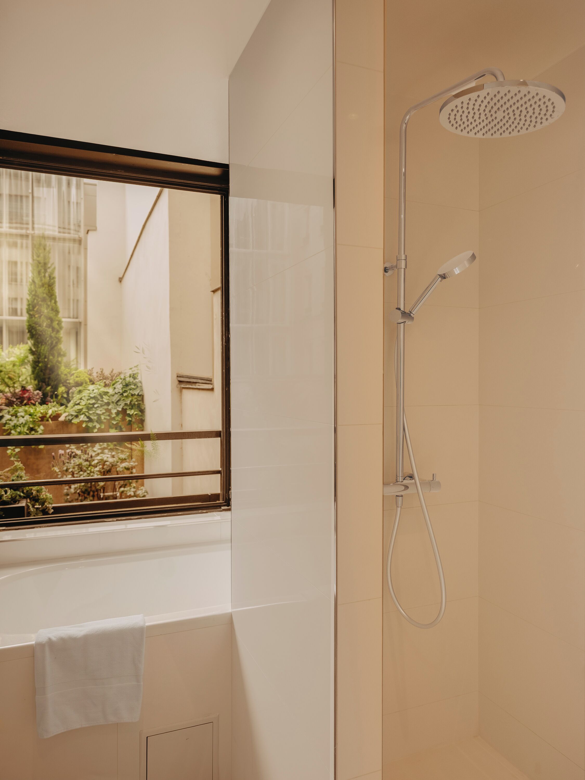 Ein Badezimmer mit Dusche, einem Fenster mit Blick auf Grünflächen und einem Handtuch an der Wand.