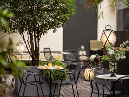 An outdoor seating area with tables and chairs, a tree, and decorative lanterns.