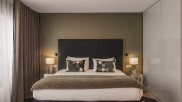 Quarto de hotel com uma cama grande, duas mesas de cabeceira, um painel de cabeceira escuro e um guarda-roupa.