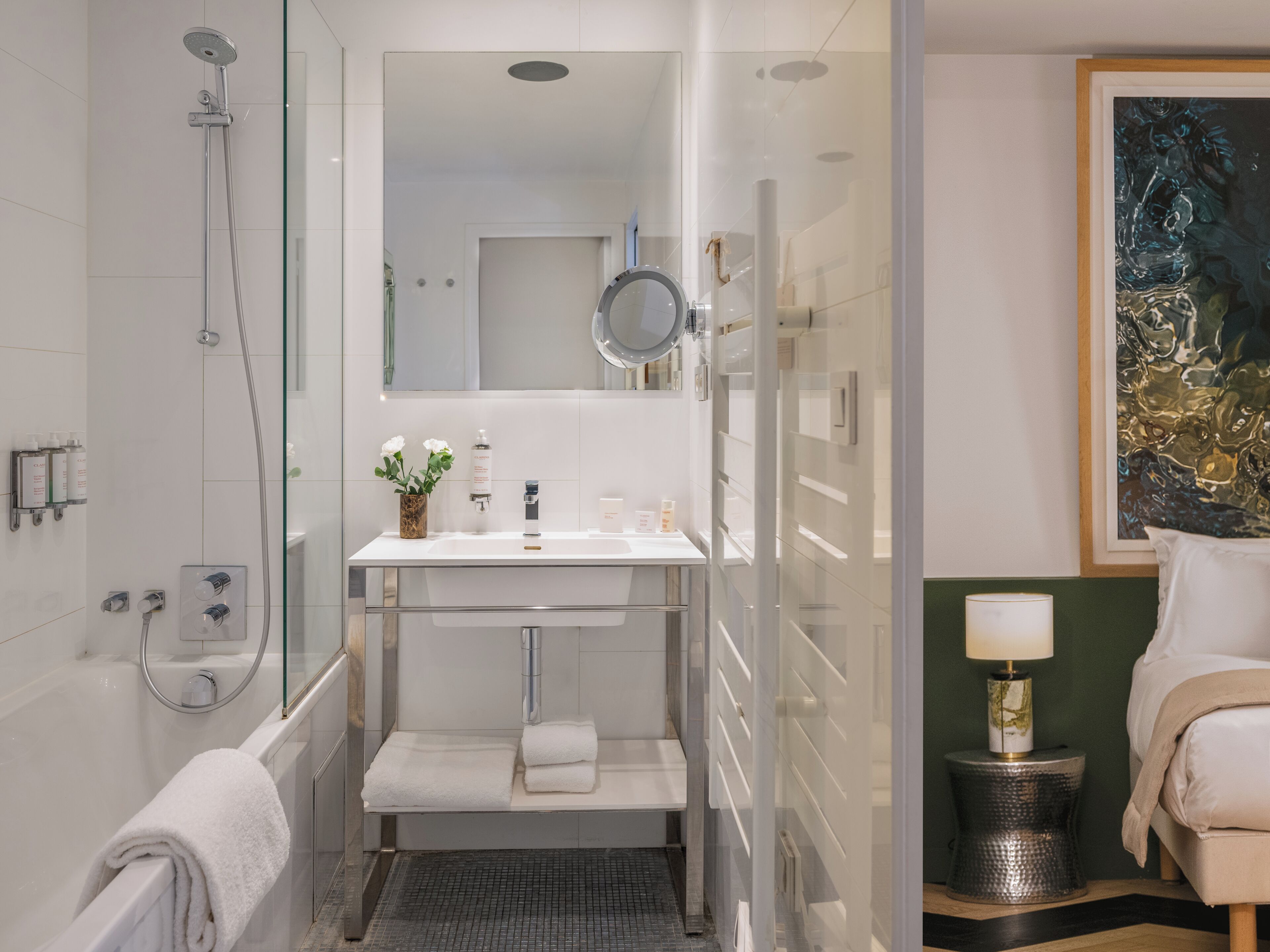 A modern bathroom with a glass shower enclosure, a white sink with a mirror above, and a small step leading to a shower.