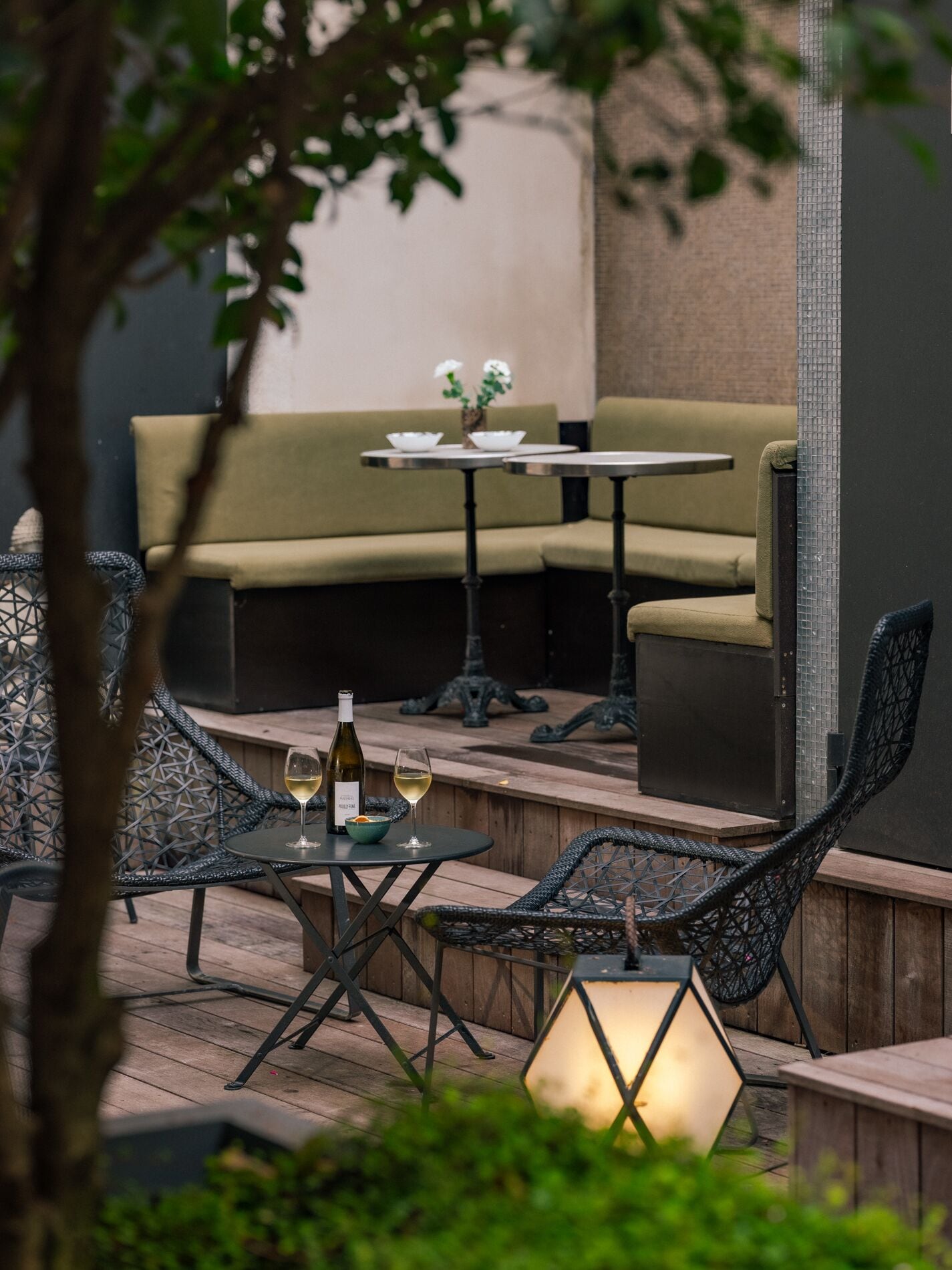 An outdoor seating area with wicker chairs, a wooden table, and a small table with a bottle of wine and glasses.