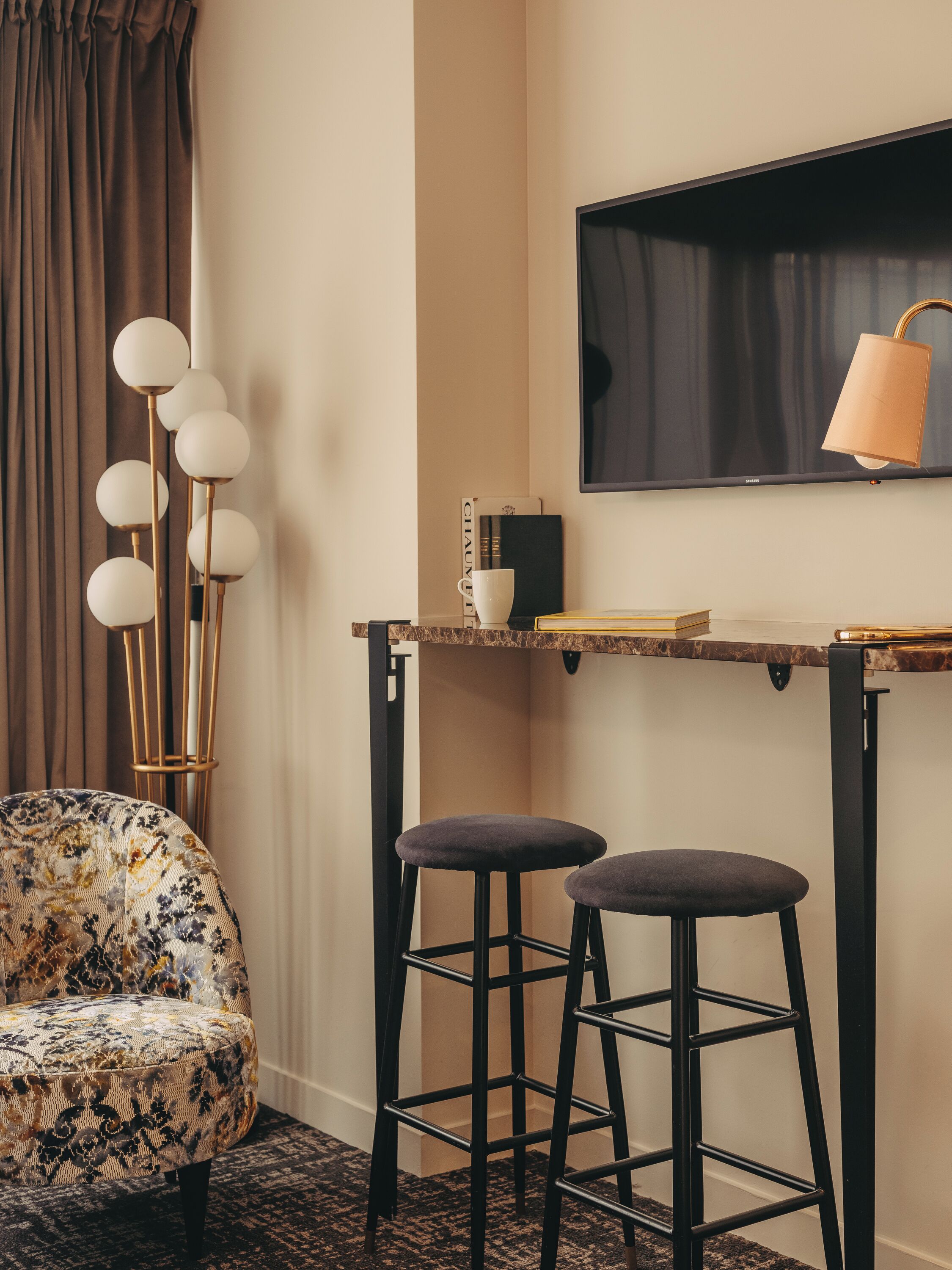 A corner room with a sofa, two bar stools, a TV, a lamp, and a bookshelf.