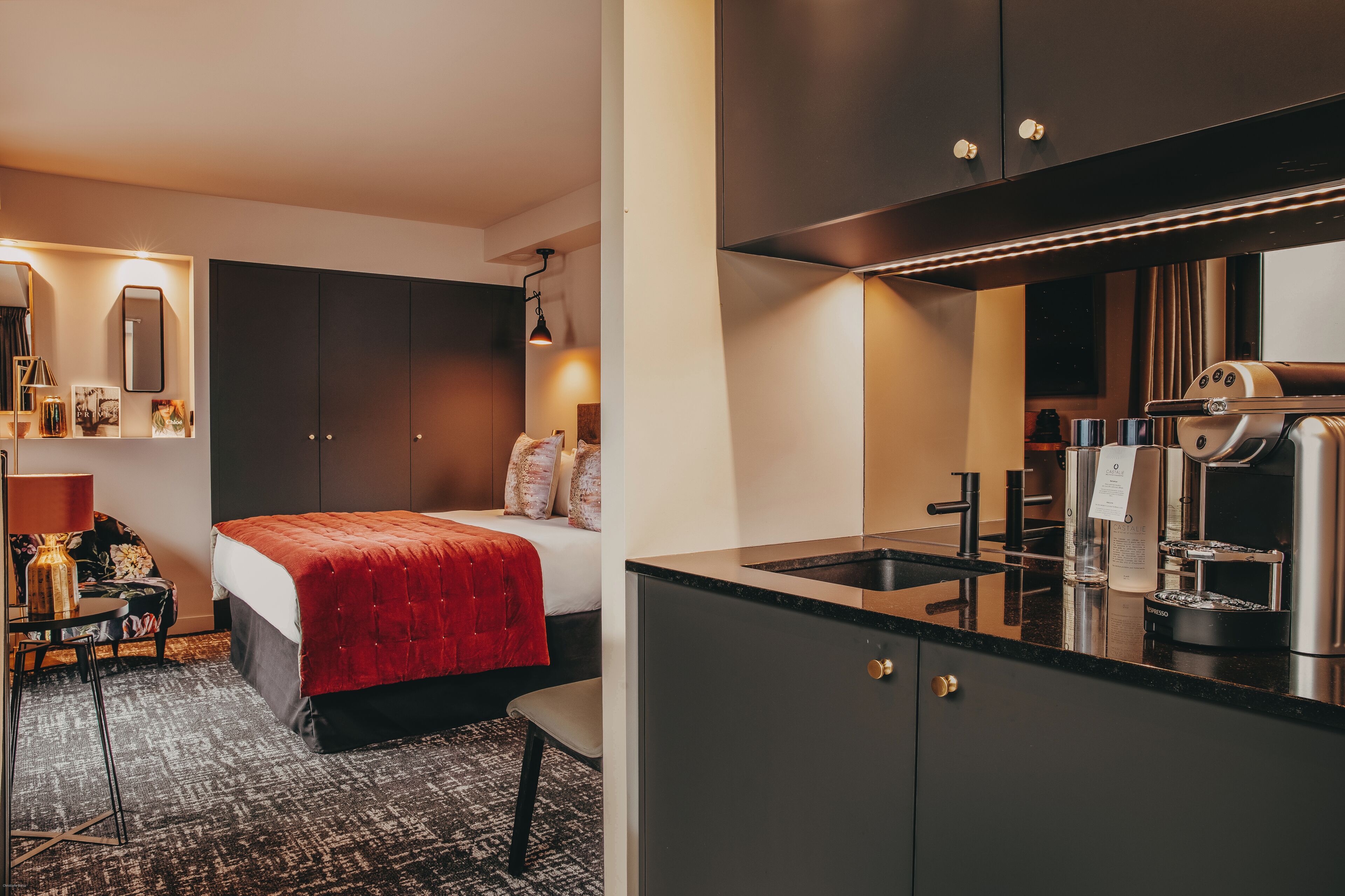 Una habitación de hotel moderna con cama, escritorio, silla, kitchenette pequeño y espejo.