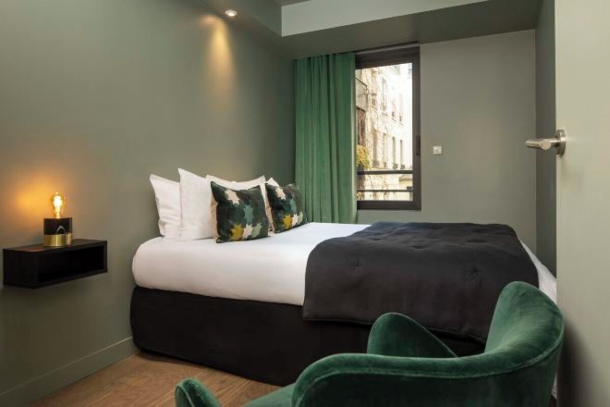 A modern bedroom with a bed, green curtains, and a nightstand with a lamp.