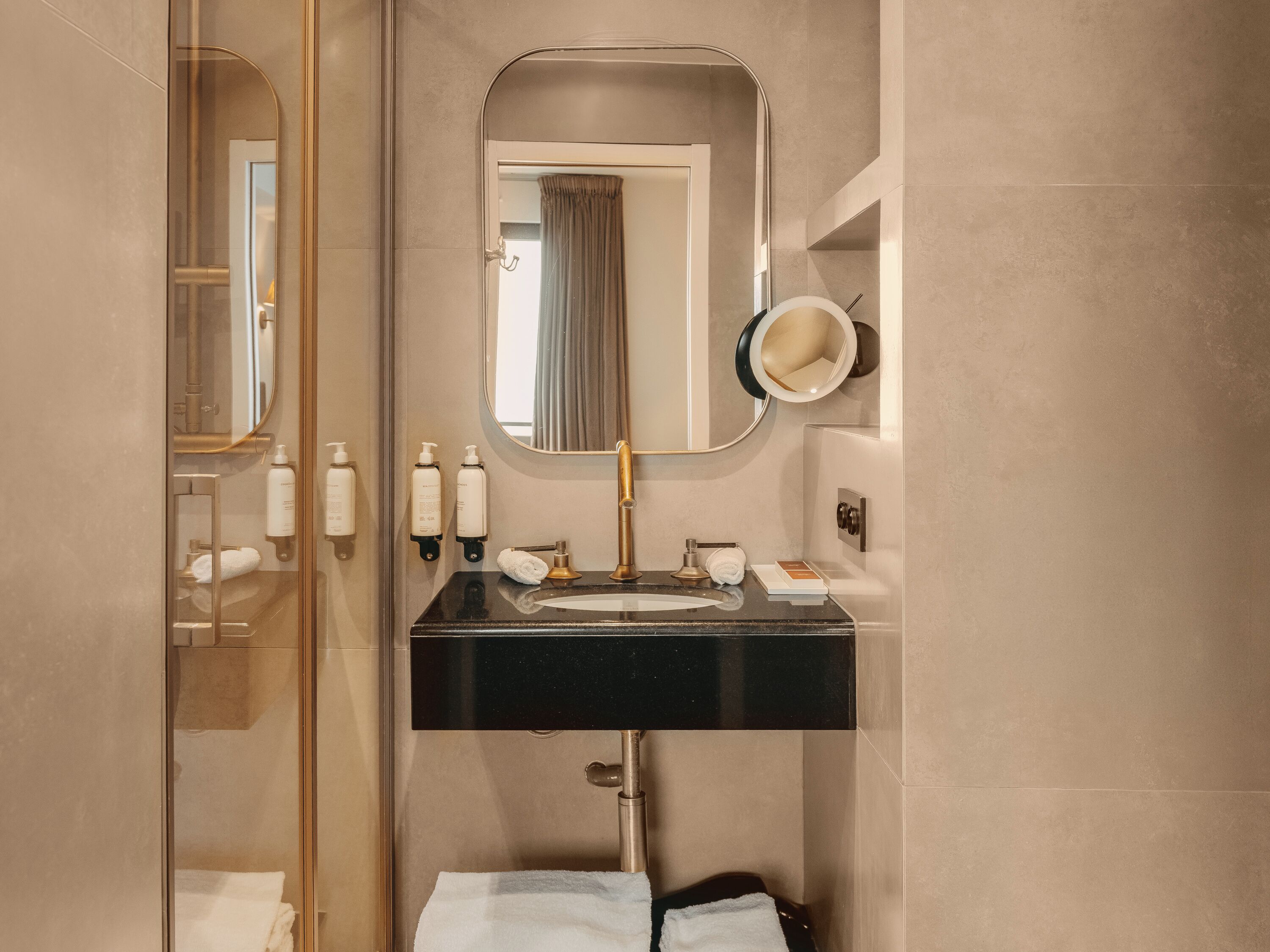 A modern bathroom with a black sink, gold fixtures, a large mirror, and a towel rack.