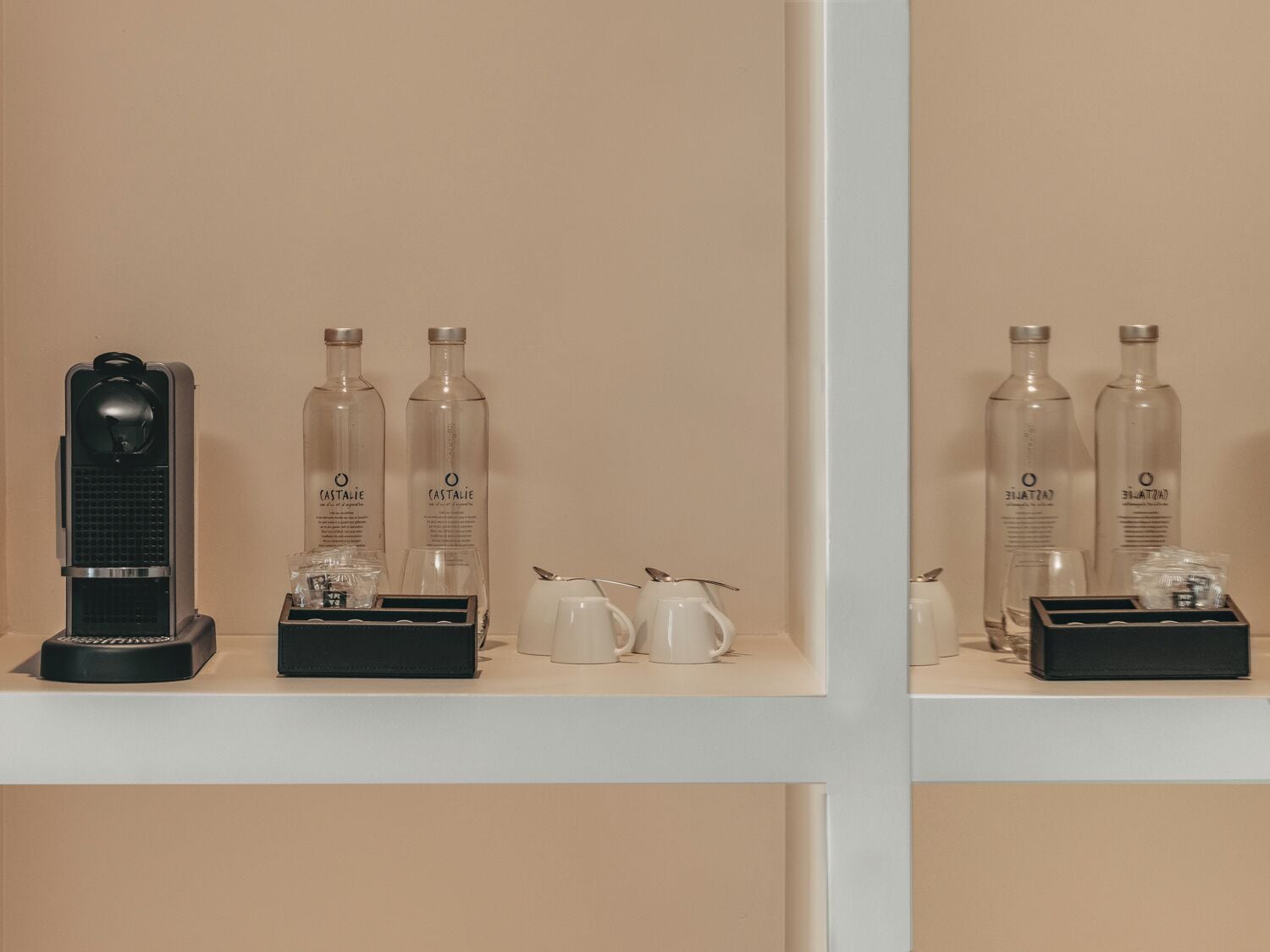 A hotel room with a minibar, two bottles of Castalie, a coffee maker, and a tea set.