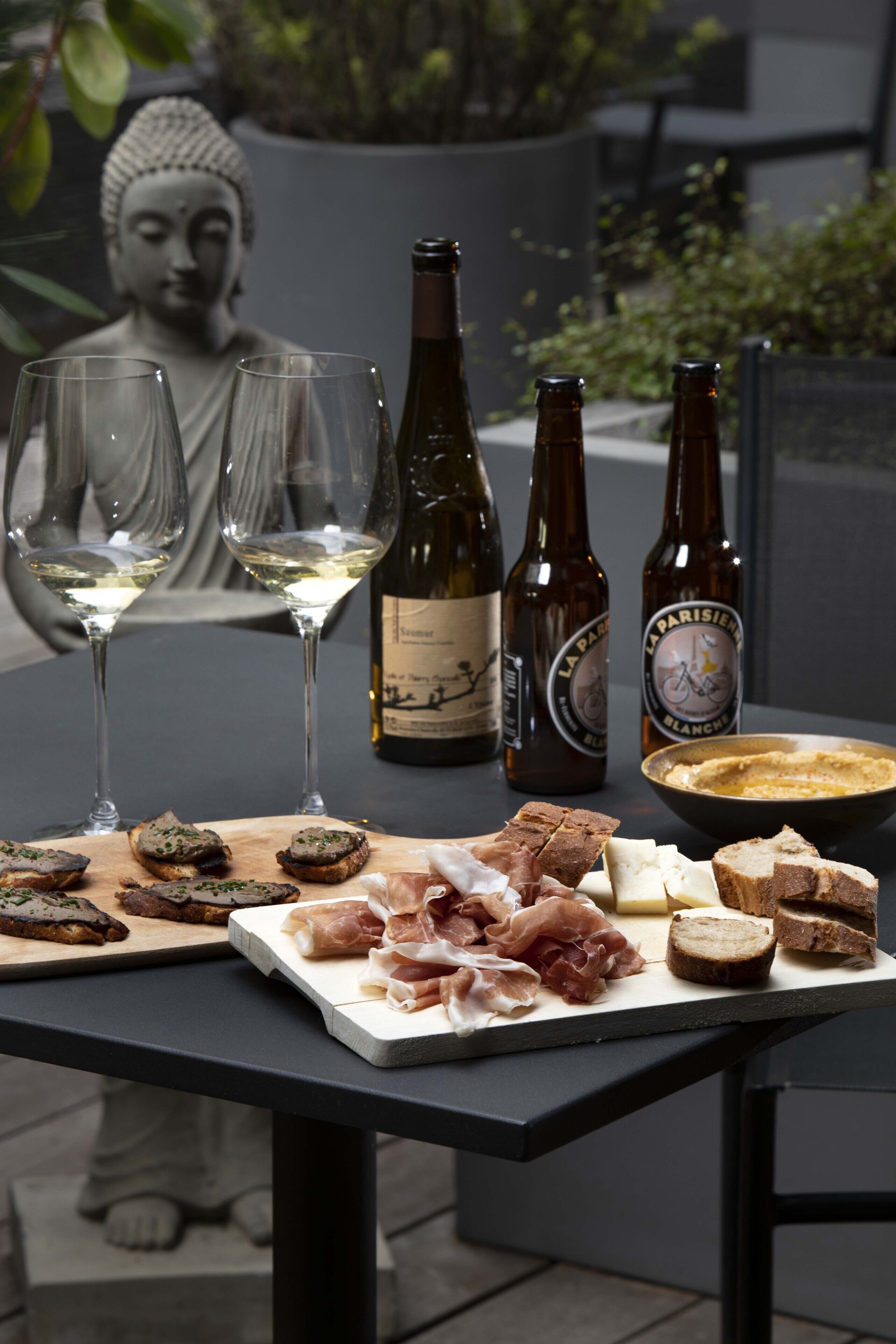 A table with wine glasses, bottles, and a variety of food including bread and meats.