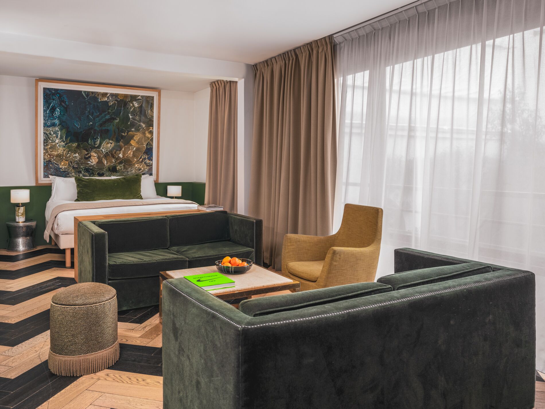 Een hotelkamer met een bed, een groene bank, een houten salontafel, een groene fauteuil en een schilderij aan de muur.