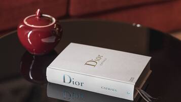 A book titled 'Dior Catwalk' on a black table with a red teapot beside it.