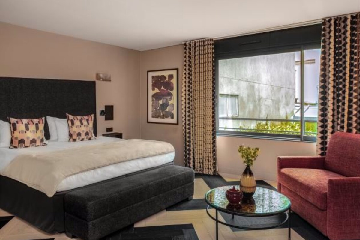 A hotel room with a large bed, a small sofa, a glass coffee table, and a window with curtains.