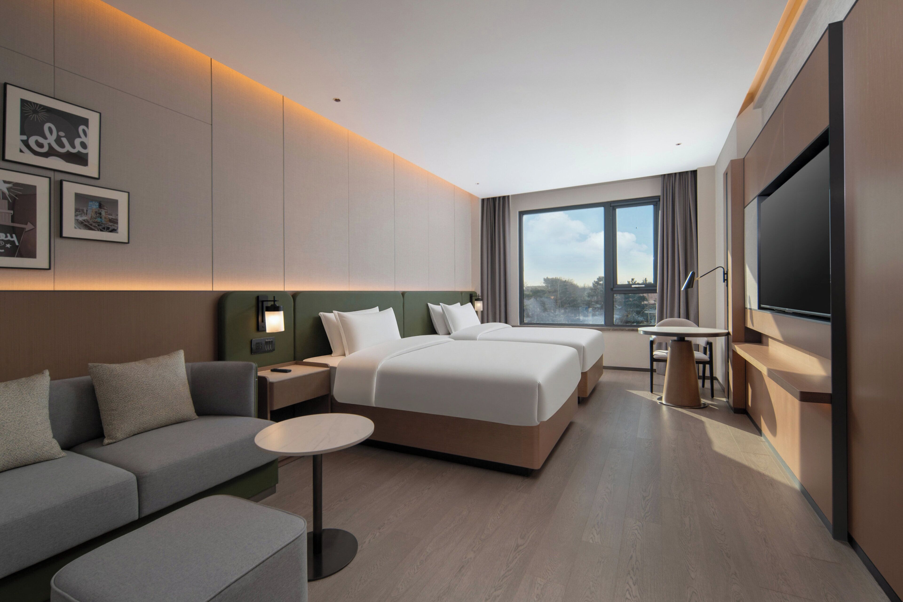 A modern hotel room with a large bed, a sofa, a desk, and a TV.