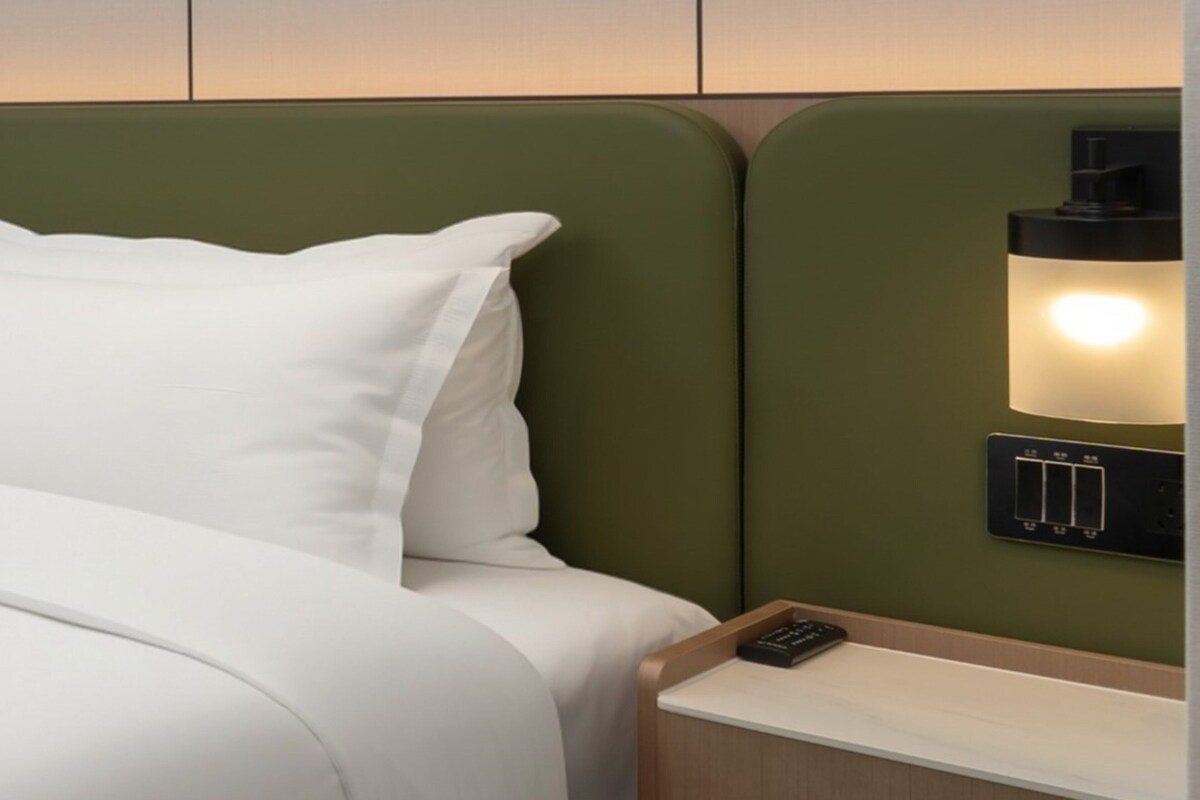 A bed with white bedding, a green headboard, and a bedside table with a remote control.