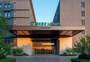 A modern hotel entrance with a large sign above the doors, a covered entrance area, and a well-maintained outdoor space with greenery. - Holiday Inn Beijing Daxing Movie Park by IHG (Daxing)