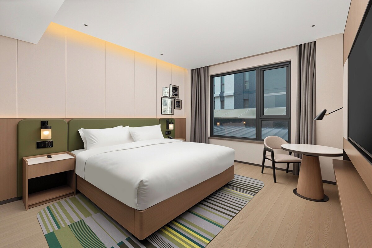A hotel room with a large bed, bedside tables, a desk, and a chair.