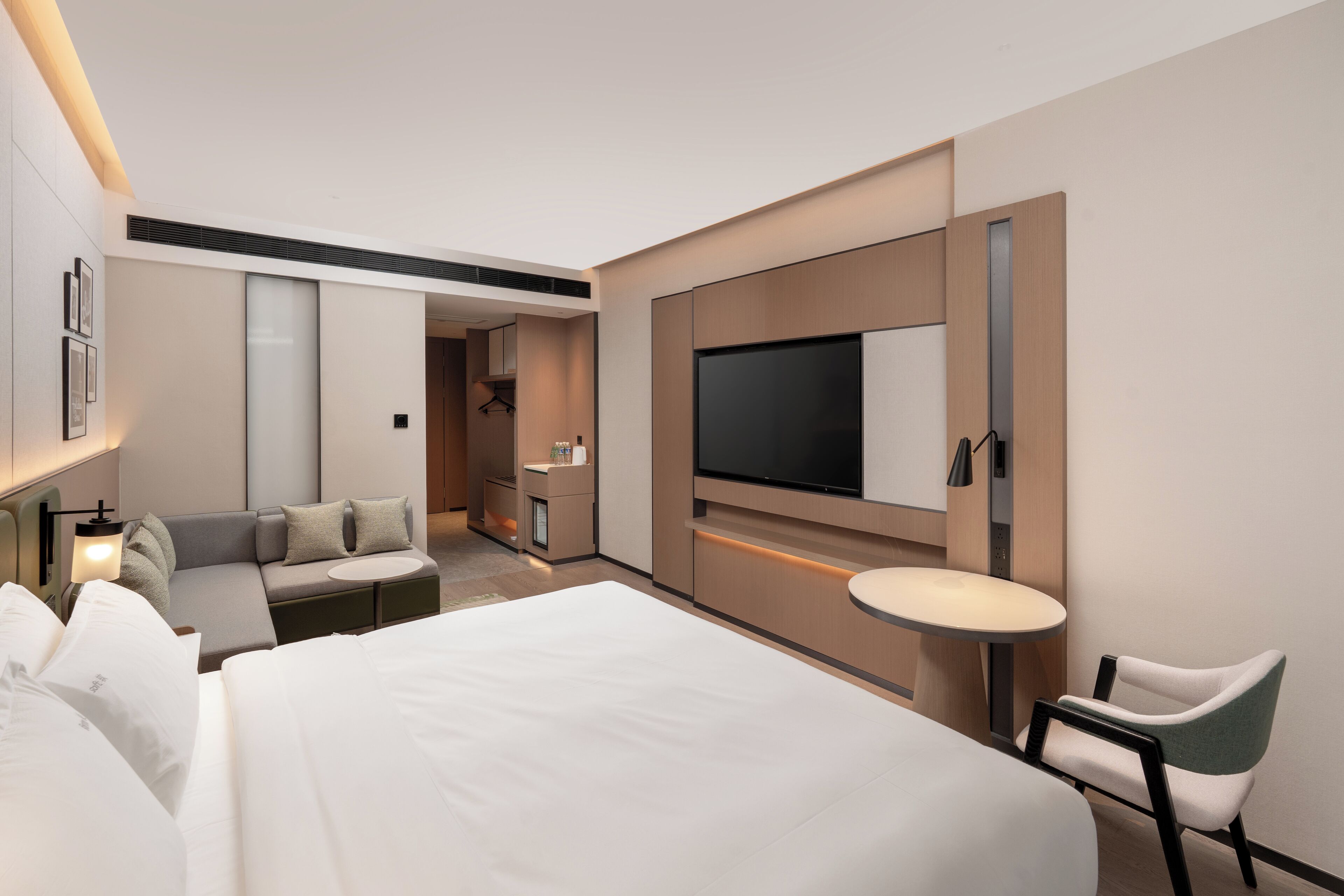 Una habitación de hotel moderna con una cama grande, un sofá, un televisor montado en la pared, una mesita y una silla.