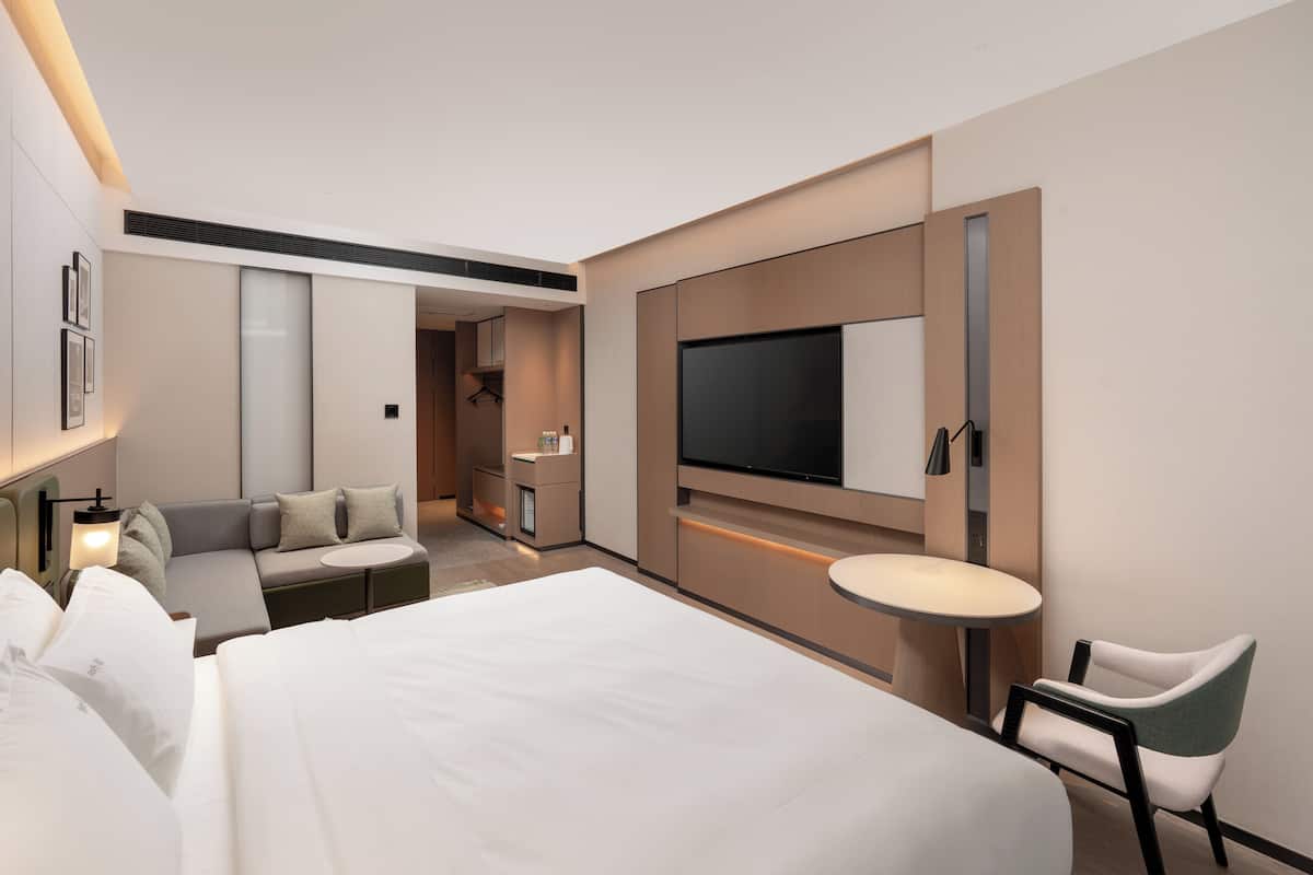Una habitación de hotel moderna con una cama grande, un sofá, un televisor montado en la pared, una mesita y una silla.