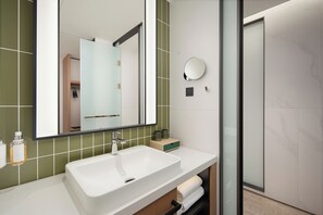 A modern bathroom with a white sink, green tiles, a large mirror, and a glass shower enclosure.