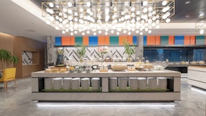 A modern buffet setup with a central island, a variety of food items, and a decorative ceiling light fixture. - Holiday Inn Beijing Daxing Movie Park by IHG (Daxing)