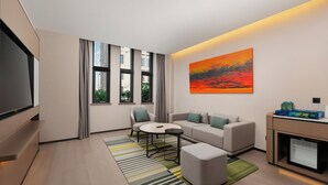 A modern living room with a flat-screen TV, a sofa, a coffee table, and a painting on the wall. - Holiday Inn Beijing Daxing Movie Park by IHG (Daxing)