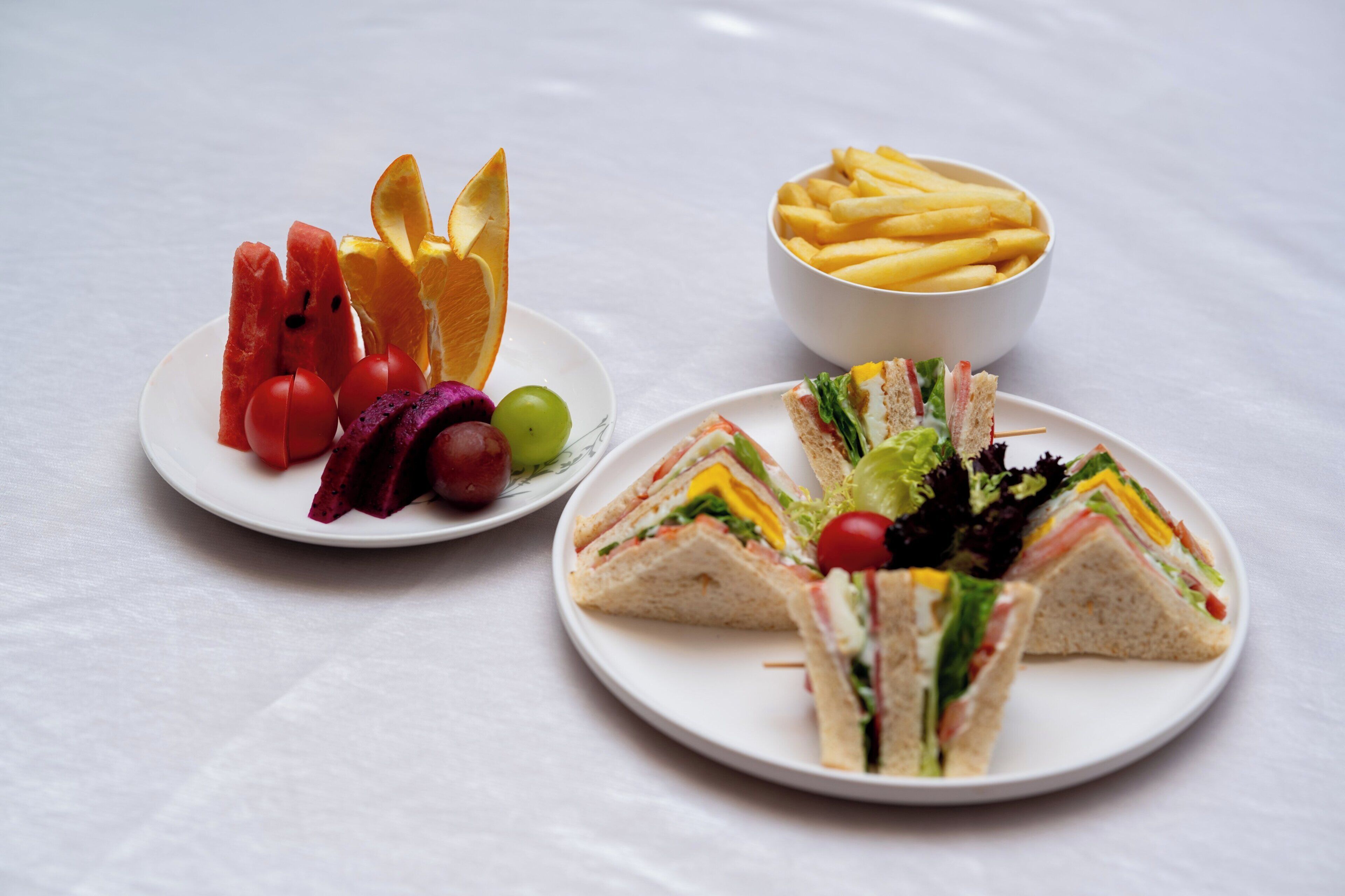 Two plates of food, one with sandwiches and vegetables, and the other with fruit and fries.
