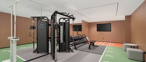 A modern gym with cardio equipment, weight machines, and a TV screen on the wall.