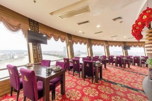 A restaurant with a panoramic view, featuring round tables and purple chairs, and a red carpeted floor.