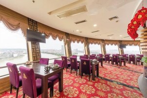 Un restaurante con vistas panorámicas, que cuenta con mesas redondas y sillas moradas, además de un suelo con alfombra roja.