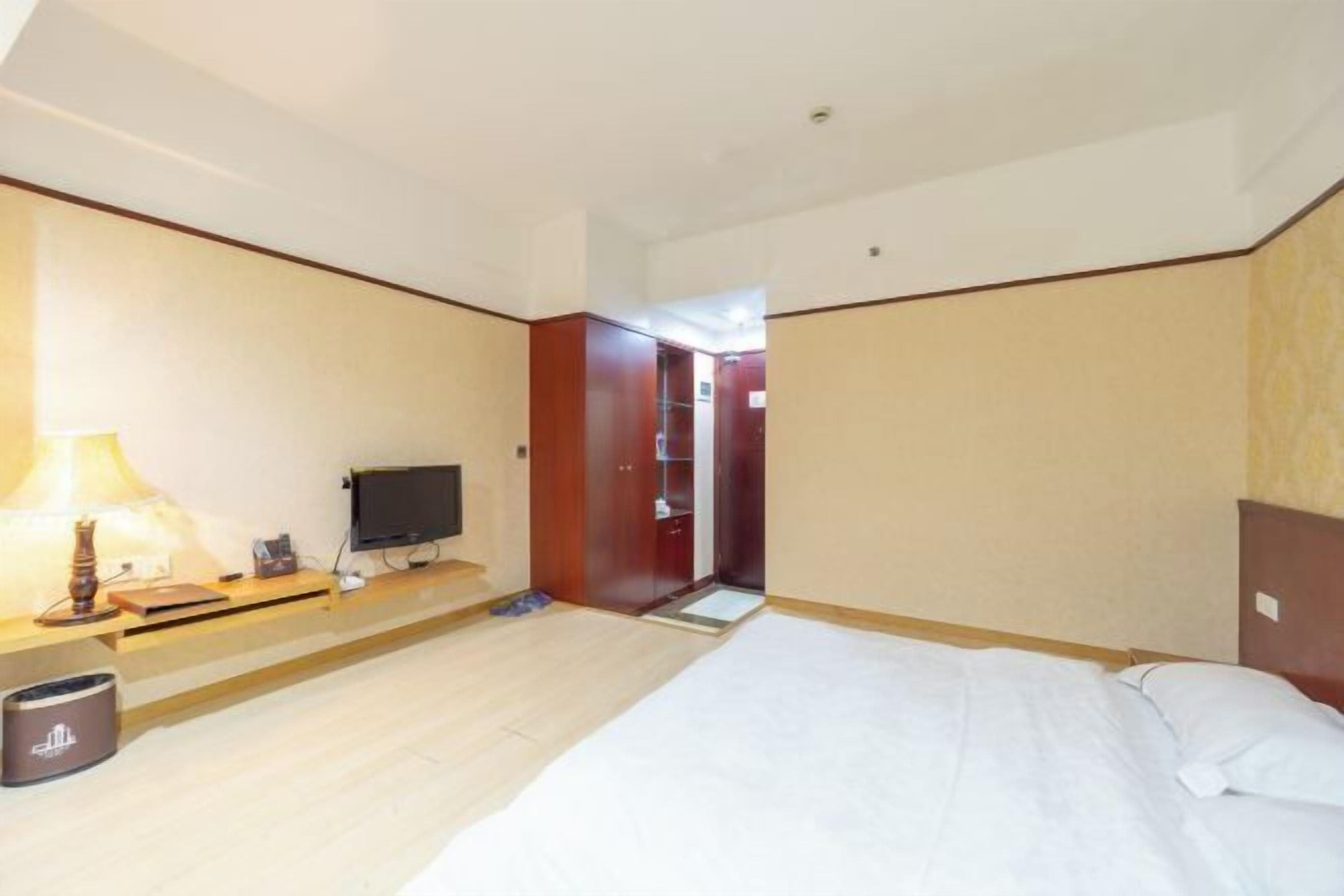 A hotel room with a bed, a TV, a desk with a lamp, and a wardrobe.