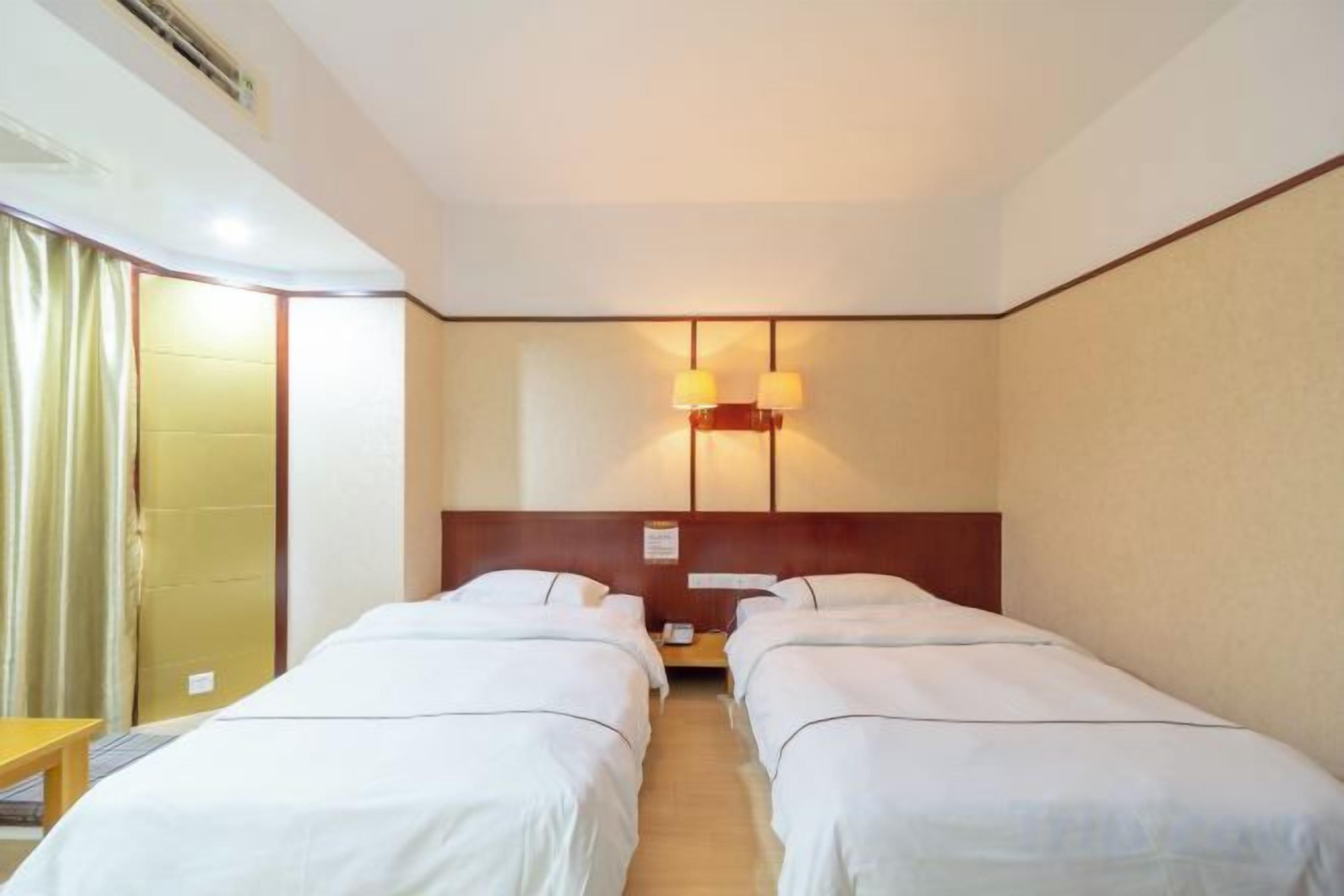 Une chambre d’hôtel avec deux lits simples, une tête de lit en bois, une table de chevet et une lampe.