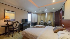 Una habitación de hotel con una cama, un escritorio con lámpara, un televisor y un espejo.