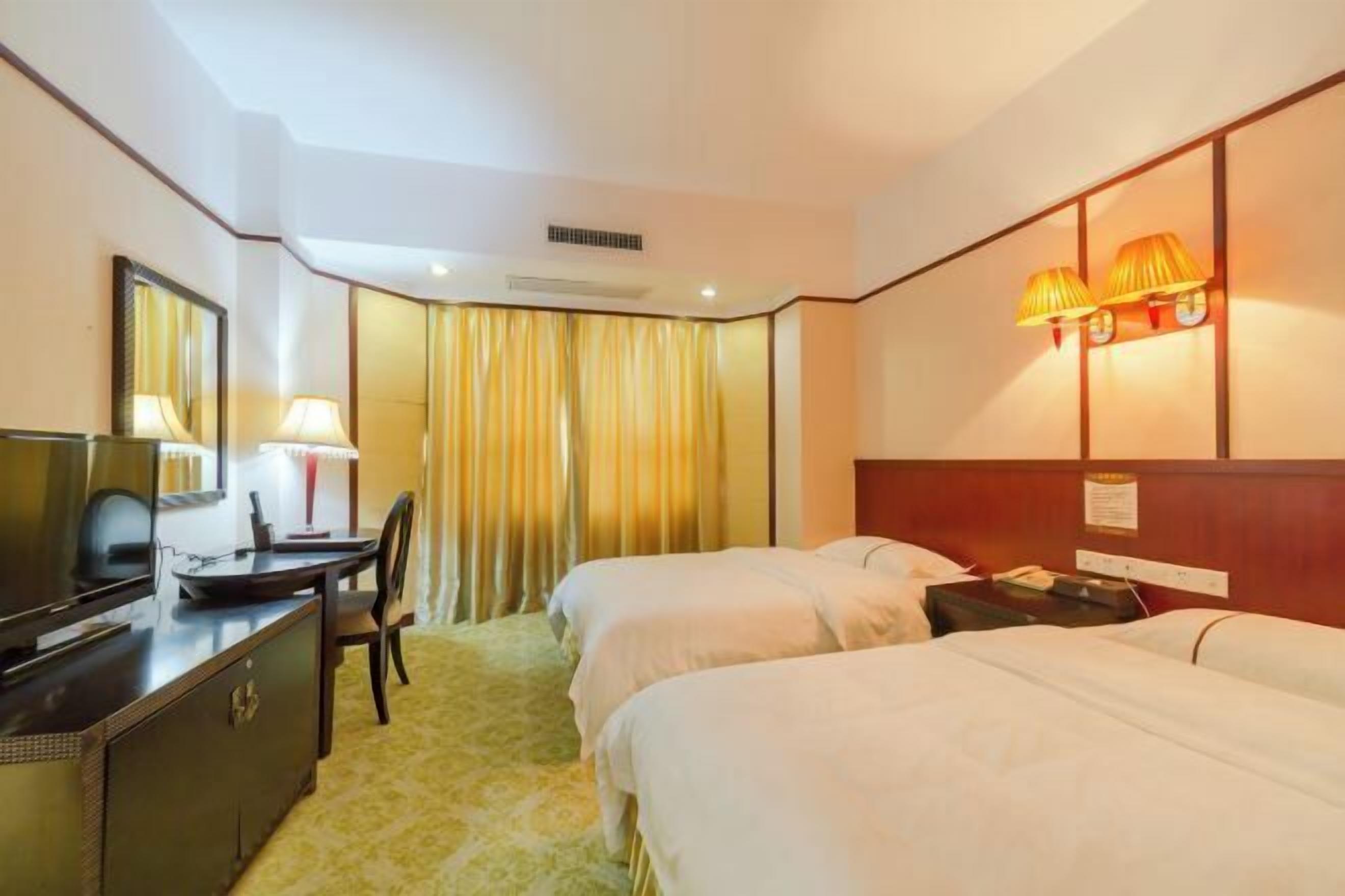 Une chambre d’hôtel avec deux lits, un bureau avec une chaise, une télévision et une lampe.