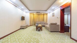 Una habitación de hotel con sofá, sillones, una mesita y televisor.