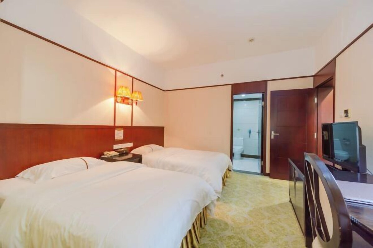 A hotel room with two beds, a desk with a television, and a bathroom visible through an open door.