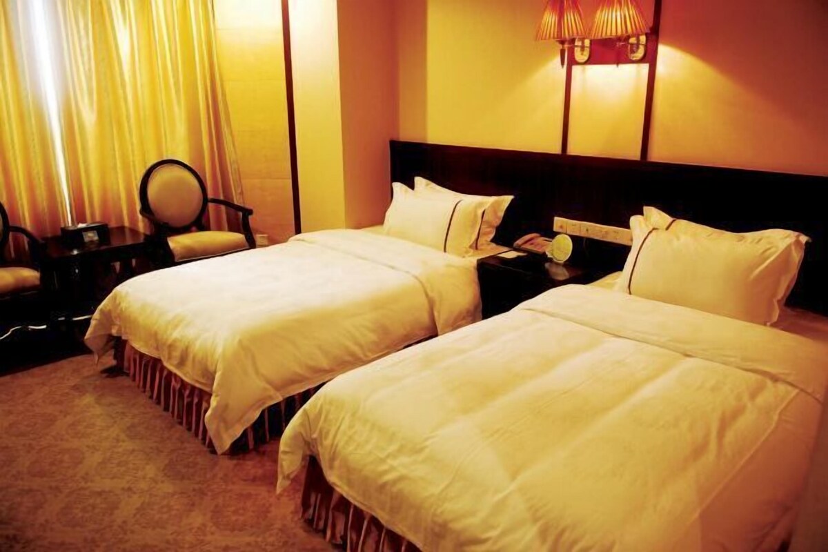 A hotel room with two beds, a nightstand, a chair, and a lamp.