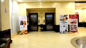 Un hall de hotel con mostrador de recepción, dos ascensores y carteles promocionales en las paredes.