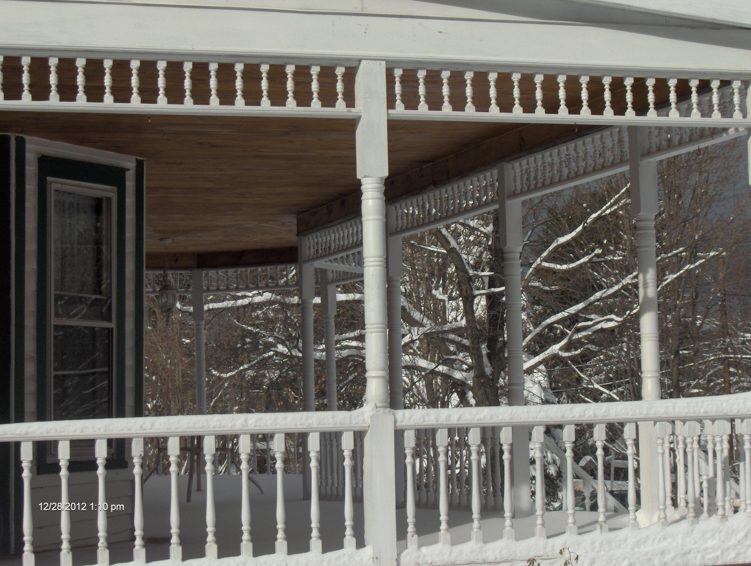 A covered porch with white balustrades and a wooden ceiling.