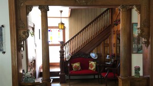 Una escalera de madera que conduce a un segundo piso, un sofá rojo con cojines florales y un piso de madera.
