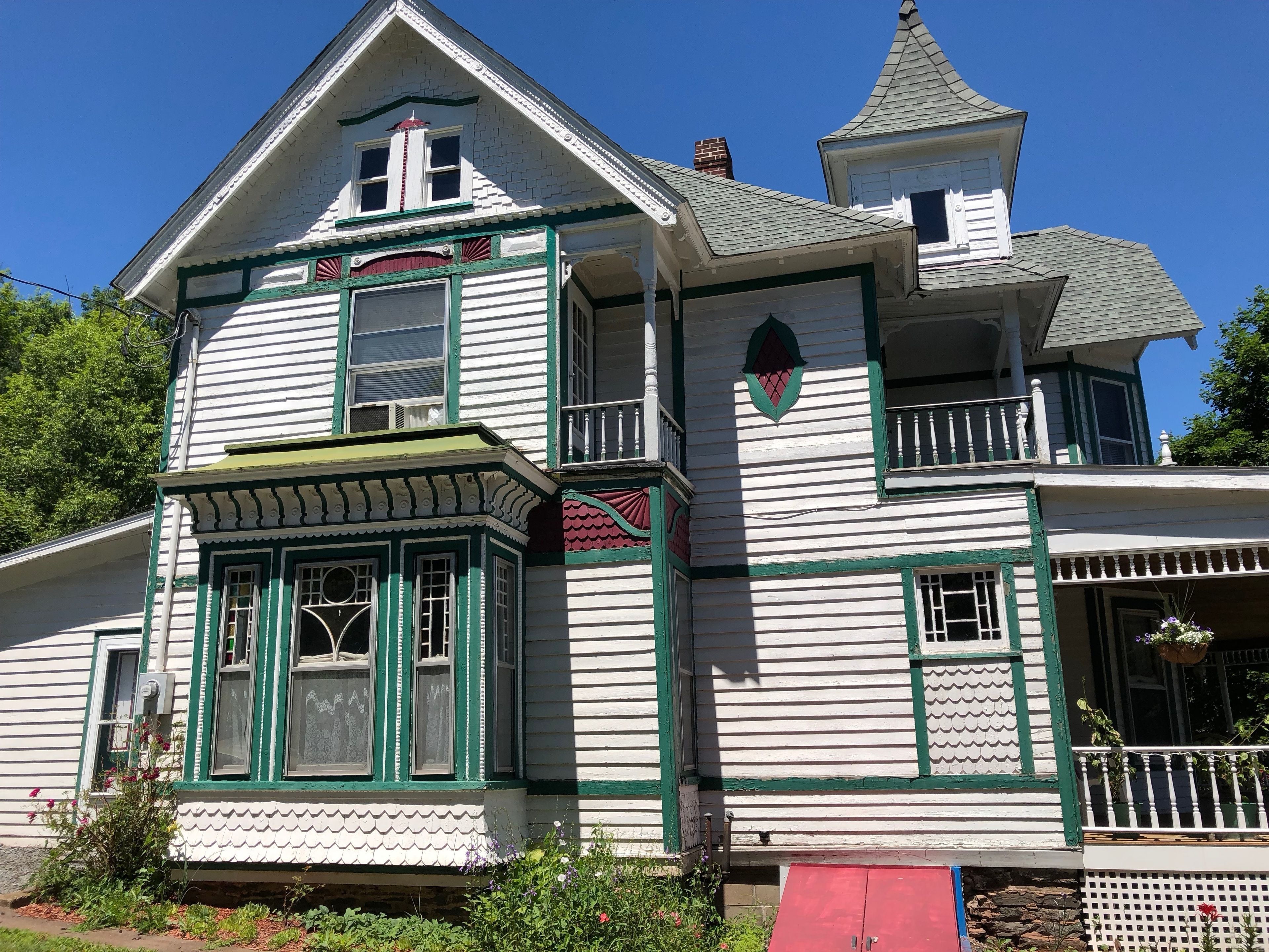 A two-story Victorian-style house with a steeply pitched roof, dormer windows, and a small tower-like structure on the roof.