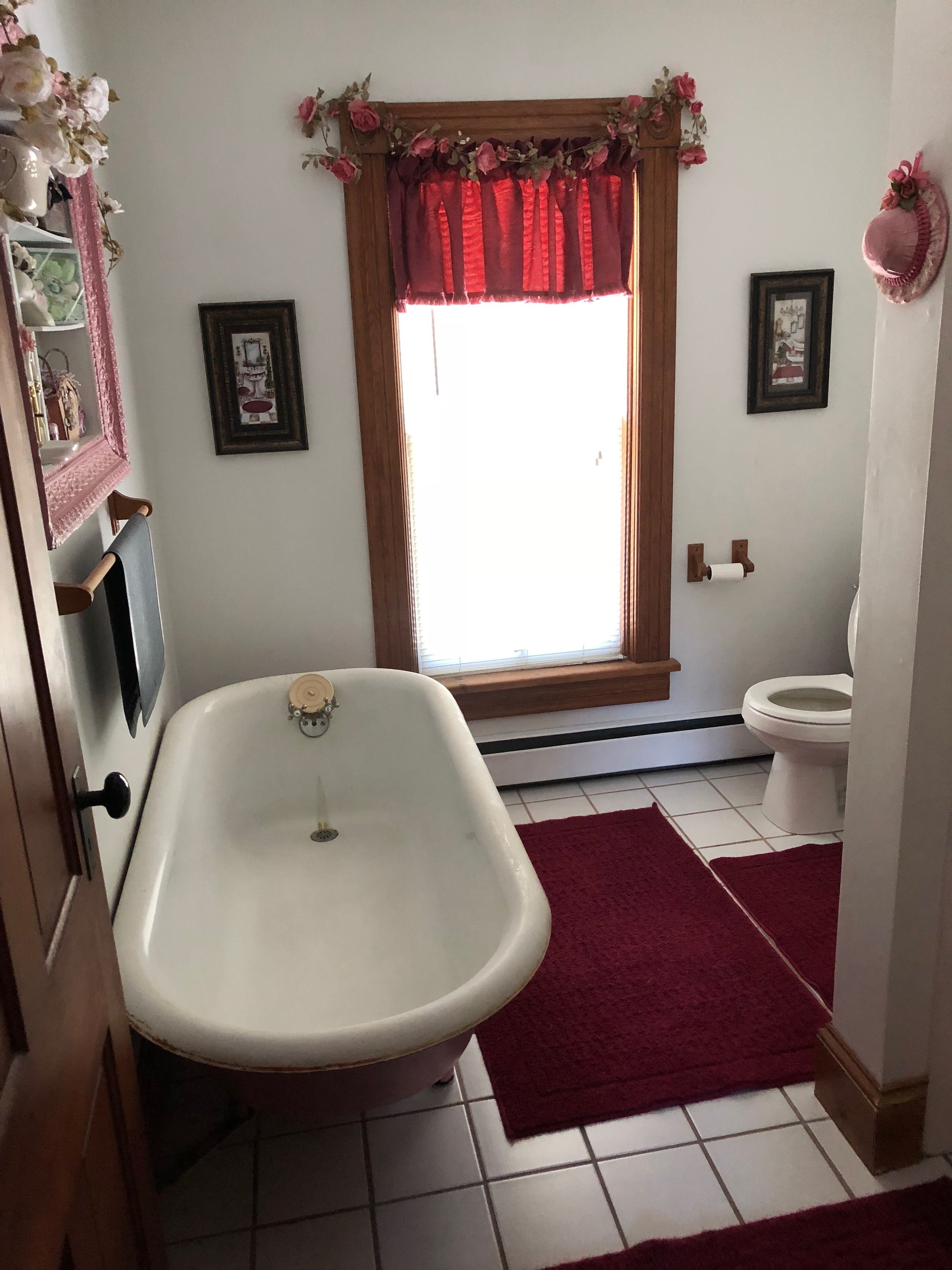 A bathroom with a white bathtub, a toilet, and a window with a red valance.