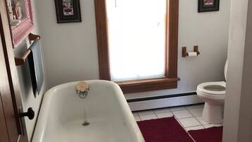 Un bagno con una vasca da bagno bianca, un water e una finestra con una tenda rossa.