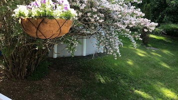 Un jardin avec une balustrade blanche, une jardinière suspendue et un arbre en fleurs.