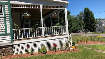 Ein zweigeschossiges Haus mit überdachter Veranda, weißem Zaun und einem Garten mit Blumen und Sträuchern.