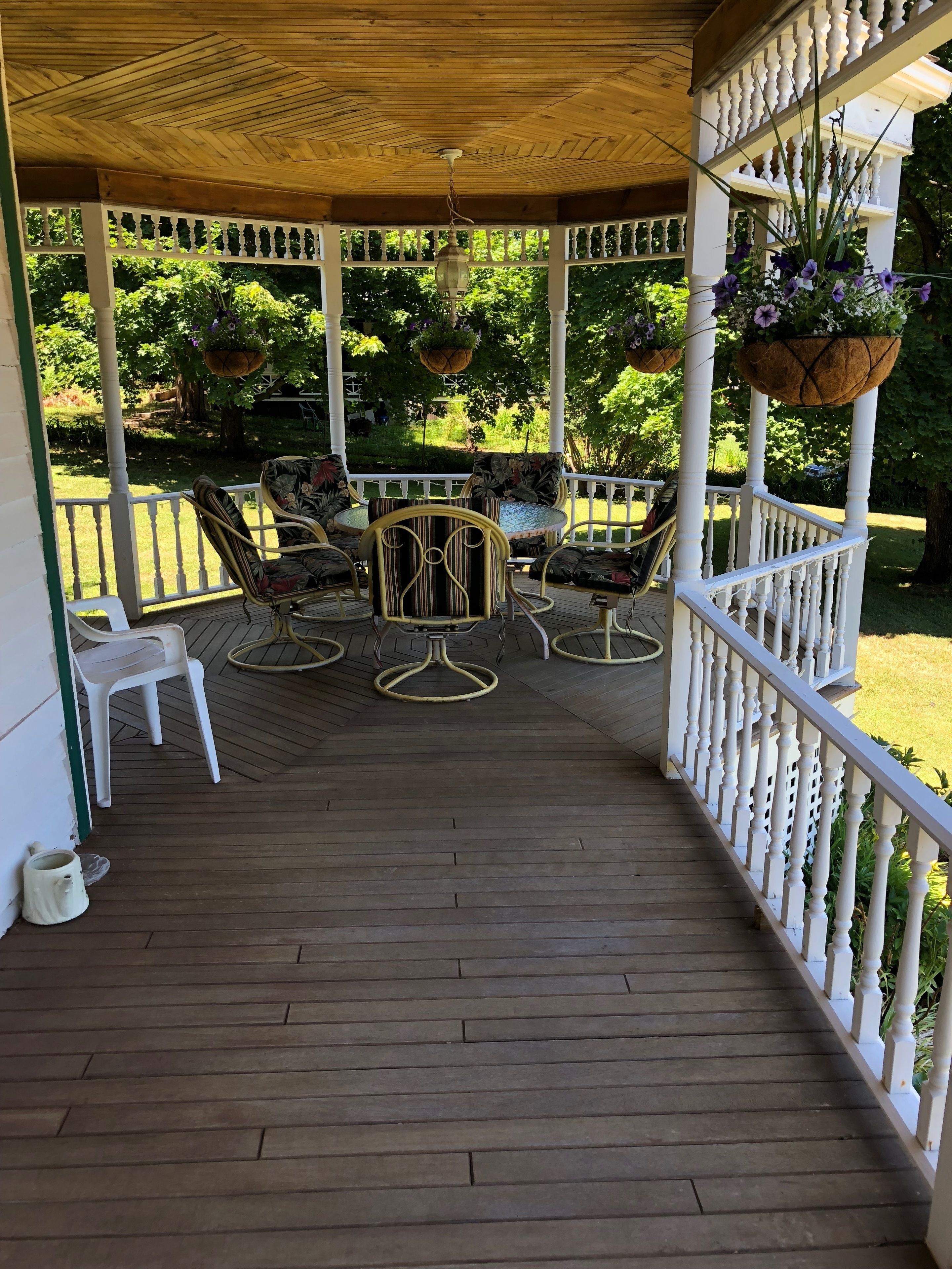 A covered porch with a wooden floor, white railings, and a seating area with chairs and a table.
