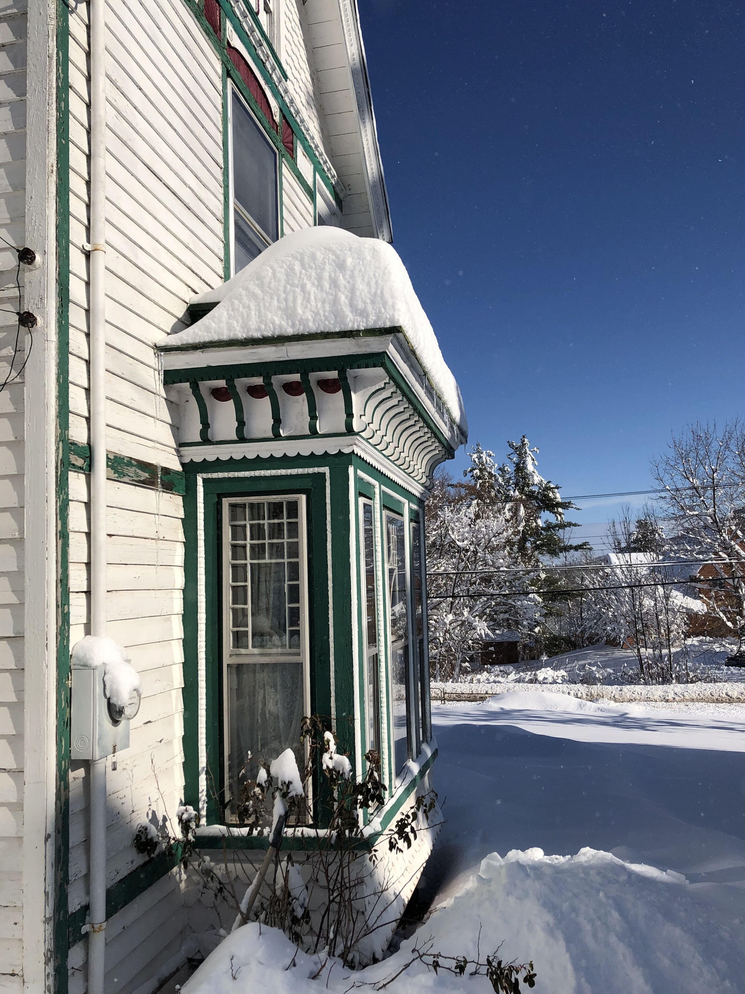 A snow-covered house with a green and white exterior, a small porch, and a clear blue sky.
