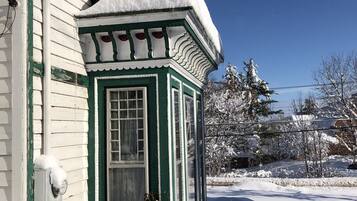 A snow-covered house with a green and white exterior, a small porch, and a clear blue sky.