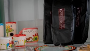 Ceramic mugs with colorful designs and text, a black velvet bag with a label, and a beaded necklace on a reflective surface. - Hotel Portal del Milán (Manizales)