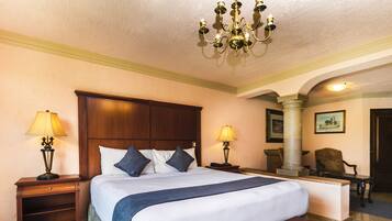 A hotel room with a large bed, two bedside tables with lamps, a bench, a chair, and a chandelier.