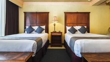 Quarto de hotel com duas camas, uma mesa de cabeceira, uma luminária e uma janela com cortinas.