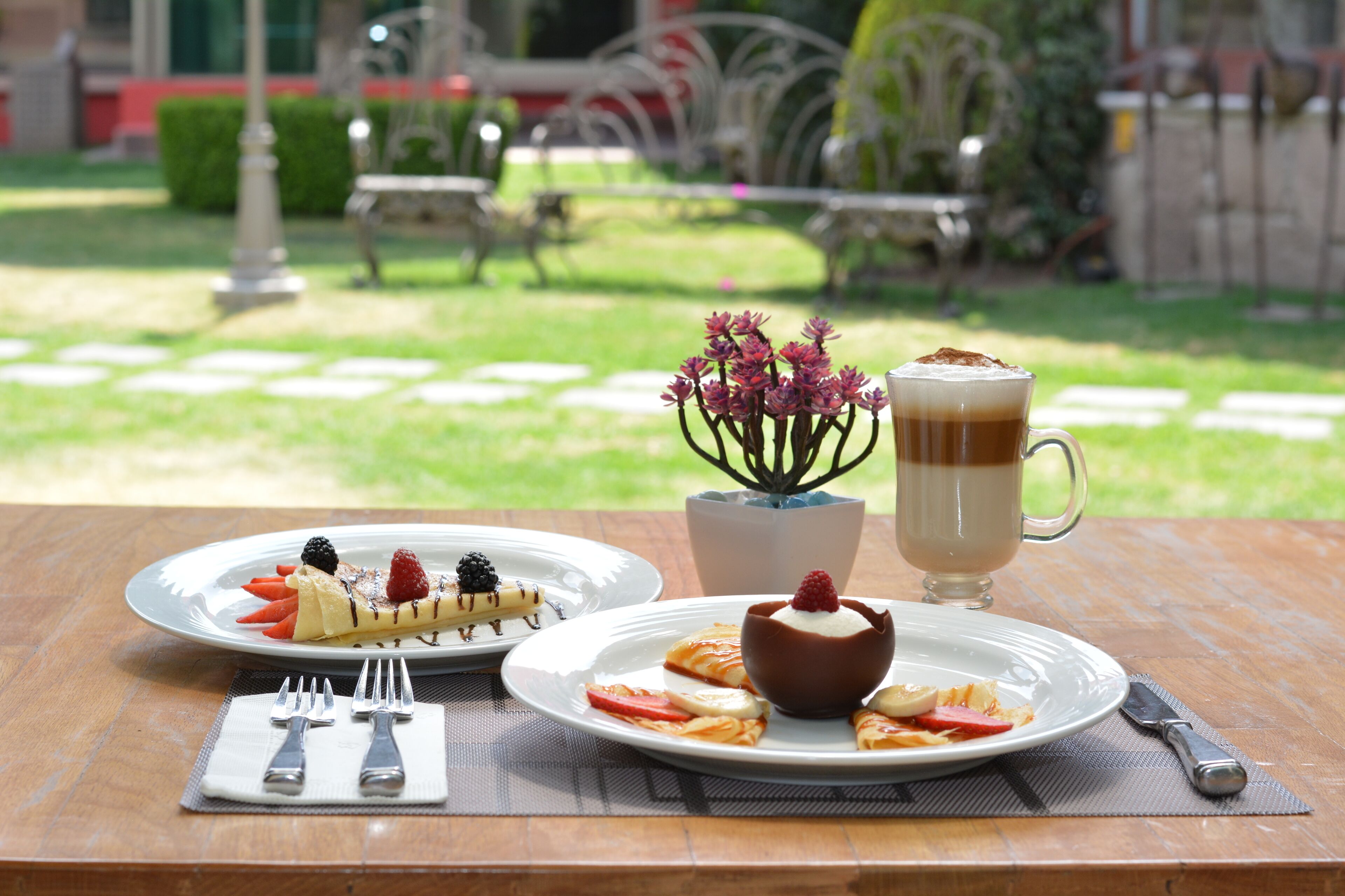 A table with two plates of dessert, a cup of coffee, and a small potted plant.